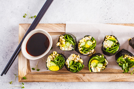https://is.gd/QslZ0OVegan green sushi rolls with avocado, sprouts, cucumber and nori on a wooden board, gray background.