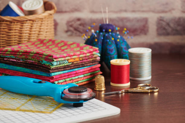 pila di tessuti colorati sul tavolo circondati da accessori da cucito su sfondo muro di mattoni - patch textile stack heap foto e immagini stock