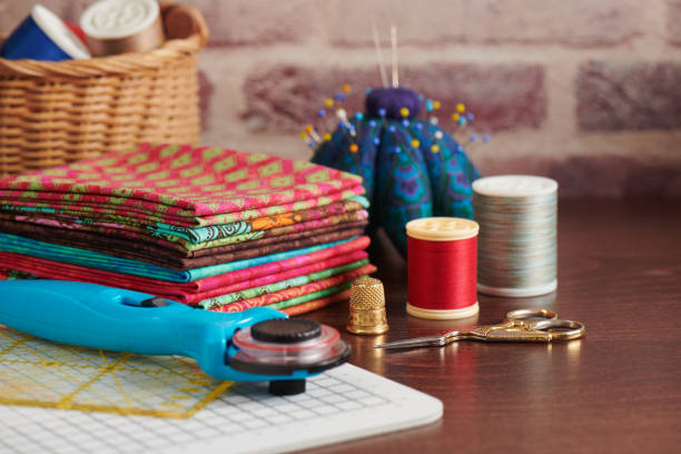 pilha de tecidos coloridos na mesa rodeada por acessórios de costura no fundo da parede de tijolo - quilt patchwork sewing textile - fotografias e filmes do acervo