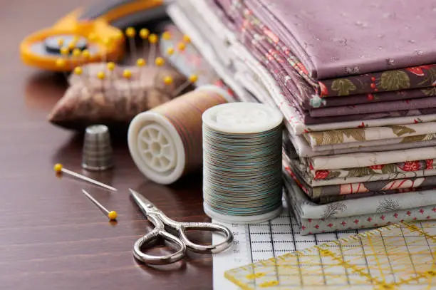 Photo of Stack of fabric for patchwork on craft mat, sewing accessories on wooden surface