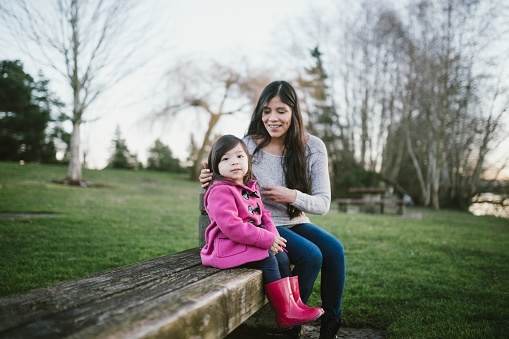 A young family spends time together at a city park in Washington State.  A mother embraces her little girl, enjoying bonding time together.