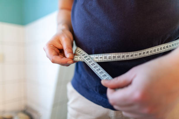 man measures her abdomen with a measuring tape - waist imagens e fotografias de stock