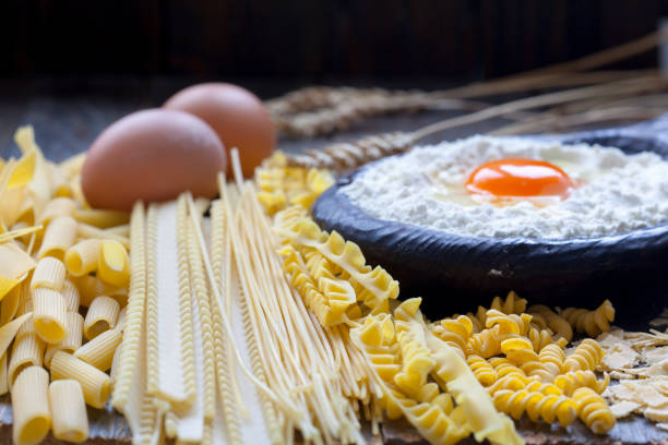 Different types of whole wheat pasta and spaghetti. Flour and egg yolk in wooden bowl.