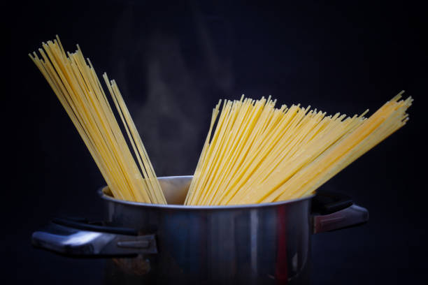 Spaghetti in pot with boiling water and steam Closeup of spaghetti in pot with boiling water and steam. Dark background. large pasta pot stock pictures, royalty-free photos & images