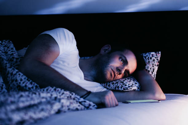 hombre joven con smartphone en la cama por la noche - working bed smart phone bedroom fotografías e imágenes de stock