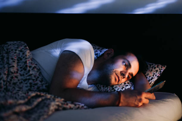 młody człowiek używający smartfona w łóżku w nocy - internet dating men chat room internet zdjęcia i obrazy z banku zdjęć