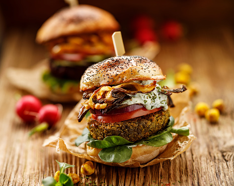 Vegetarian burgers,  homemade burger with green peas cutlet, grilled mushrooms, tomato, red onion, lamb's lettuce and yogurt and herb sauce on a wooden background. Healthy eating concept