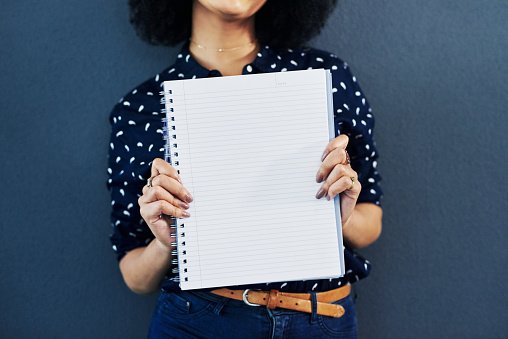 Studio shot of a young woman holding up a blank notebook against a blue background
