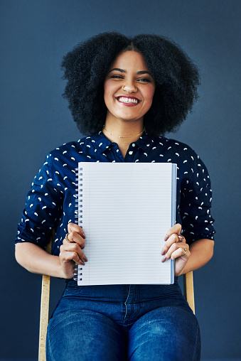 Studio shot of a young woman holding up a blank notebook against a blue background