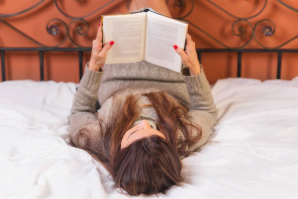 istock Woman lying in bed reading a book 1094256722