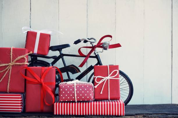 Group of elegant red gift box stack decorated with vintage toy bicycle on wood background, vibrant valentine lovely present concept, copy space stock photo