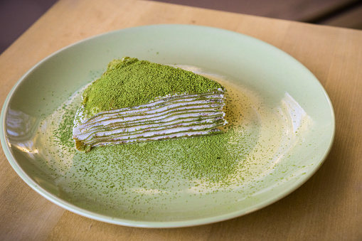 Slice of homemade Matcha mille crepe cake covered in green tea powder for presentation purposes