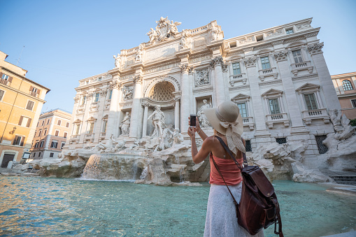 Young woman in Rome enjoying travel in Italy and capturing a photo of the Trevi fountain using her smart phone