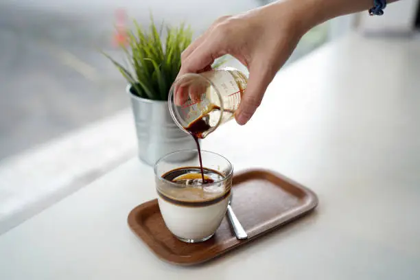 Pouring espresso shot into a glass of coconut pudding, Refreshing homemade dessert concept.