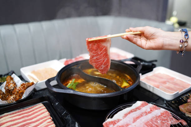 Holding raw sliced beef using chopsticks on hot pot with smoke for Japanese hot pot.