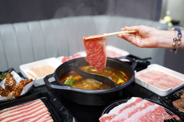 холдинг сырой нарезанной говядины с использованием палочки на горячей кастрюле с дымом для японской горячей кастрюле. - shabu стоковые фото и изображения