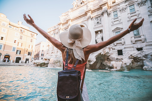 Young woman at the Trevi fountain in Rome standing arms outstretched enjoying travel freedom in Italy