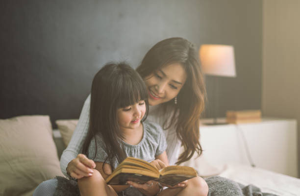 mother and daughter reading book at home in the bedroom mother and daughter reading book at home in the bedroom bedtime photos stock pictures, royalty-free photos & images