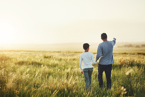 Rearview shot of a father and his son walking on a field