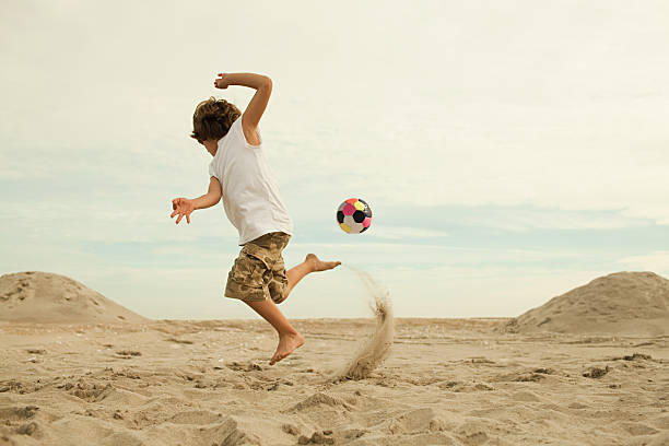 boys kicking football on beach - beach football 뉴스 사진 이미지