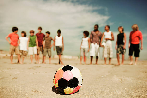 garçon debout sur la plage avec ballon de football - american football football focus on foreground team sport photos et images de collection