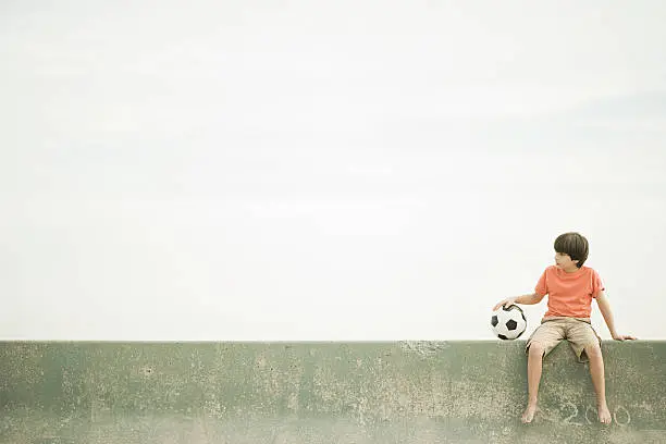Photo of Boy sitting on wall with football