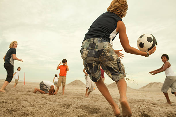 ragazzi giocare a calcio sulla spiaggia - football player group of people running american football foto e immagini stock