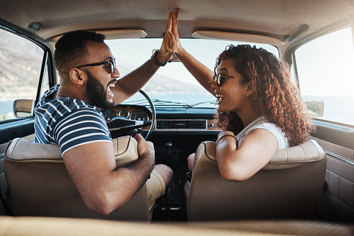Shot of a young couple giving each other a high five on a road trip