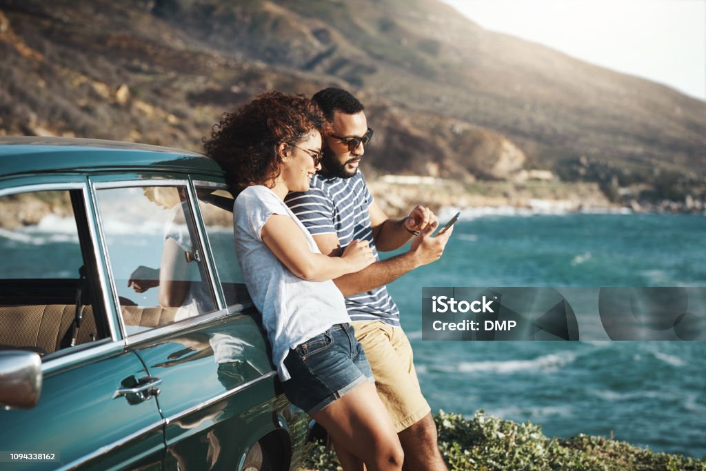 Summer's a time for adventure Shot of a young couple using a mobile phone on a road trip Car Stock Photo