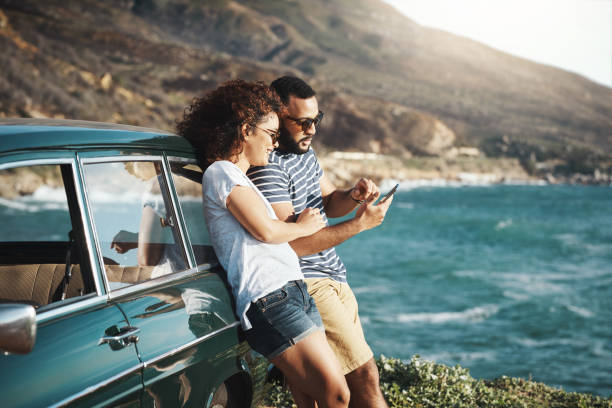 Summer's a time for adventure Shot of a young couple using a mobile phone on a road trip beach lifestyle stock pictures, royalty-free photos & images