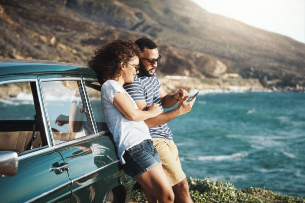 Summer's a time for adventure Shot of a young couple using a mobile phone on a road trip beach holidays stock pictures, royalty-free photos & images