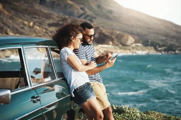 Shot of a young couple using a mobile phone on a road trip