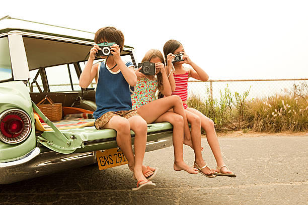 three children sitting on back of estate car taking photographs - zomer fotos stockfoto's en -beelden
