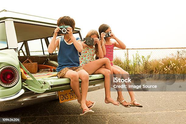 Three Children Sitting On Back Of Estate Car Taking Photographs Stock Photo - Download Image Now