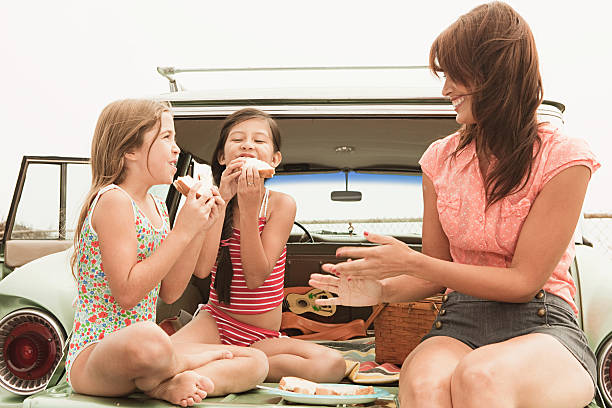 mother and daughters eating sandwiches on car boot - motor vehicle road trip western usa southern california 뉴스 사진 이미지