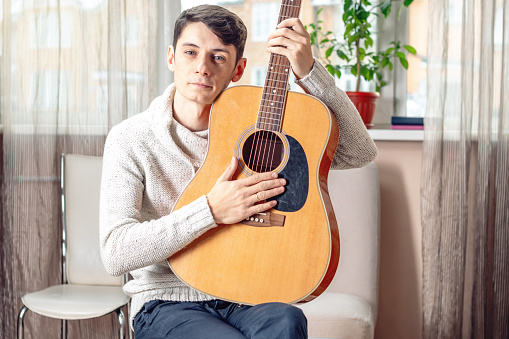 Young attractive male musician sitting on a chair holding an acoustic guitar. The concept of music as a hobby
