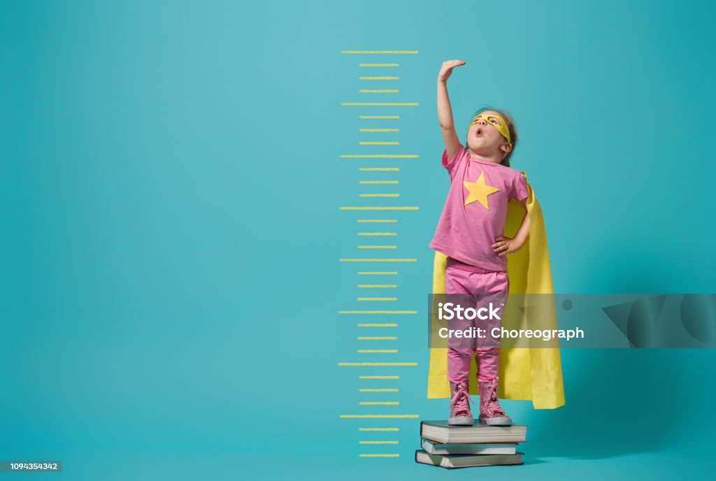 child playing superhero Little child playing superhero. Kid measures the growth on the background of bright blue wall. Girl power concept. Yellow, pink and  turquoise colors. Child Stock Photo