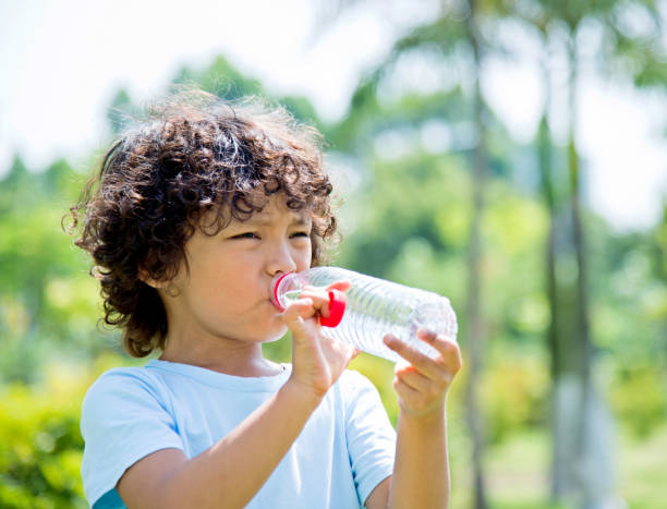 Young asian boy drinking water outdoors.