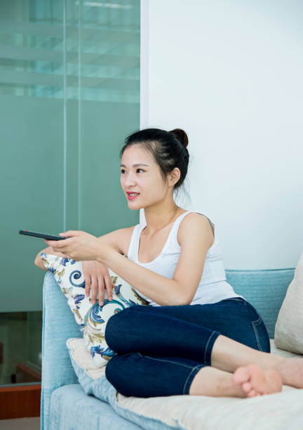 istock Young asian woman with remote control watching television on sofa 1094367754