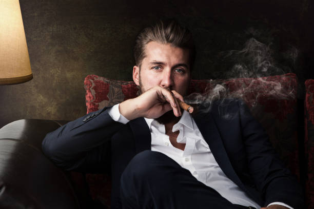 hombre de negocios atractivo con un cigarro está descansando en el sofá - símbolo sexual fotografías e imágenes de stock