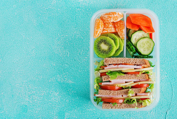schule lunchpaket mit sandwich, obst, wasser und gemüse auf tisch. gesunde ernährung gewohnheiten konzept. flach zu legen. ansicht von oben - lunch box lunch sandwich green stock-fotos und bilder