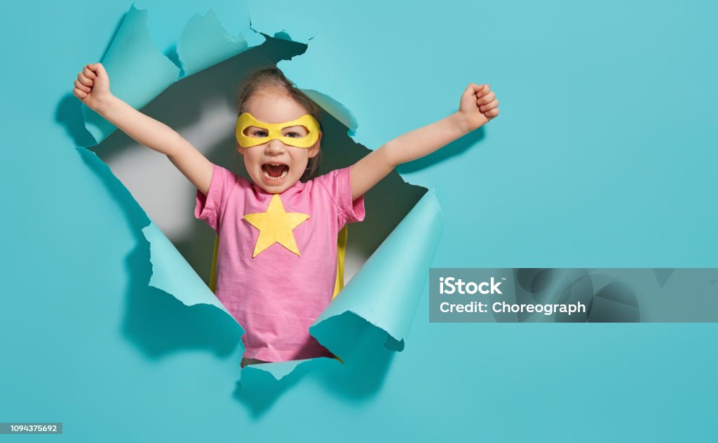 child playing superhero Little child playing superhero. Kid on the background of bright blue wall. Girl power concept. Yellow, pink and  turquoise colors. Child Stock Photo