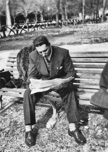 Young man reading newspaper on a bench in 1941