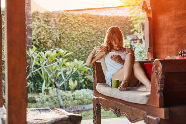 istock Cute woman using smartphone and drinking tea on a porch sofa. 1094386658