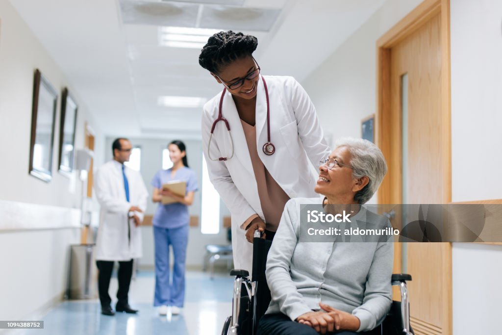 Doctora, empujando a paciente senior en silla de ruedas - Foto de stock de Paciente libre de derechos