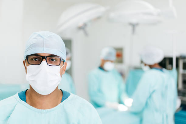 Male doctor wearing surgical mask and looking at camera A male doctor wearing a surgical mask in surgery room and looking at the camera. surgical light stock pictures, royalty-free photos & images