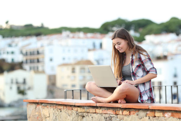 istock Teen using a laptop on a ledge in a town 1094391536