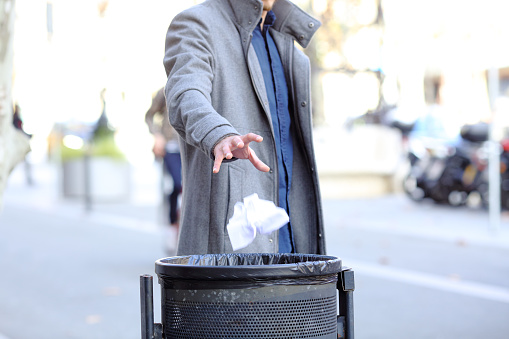 Man hand throwing paper into trash bin