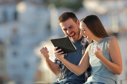 Excited couple checking tablet online content in a town