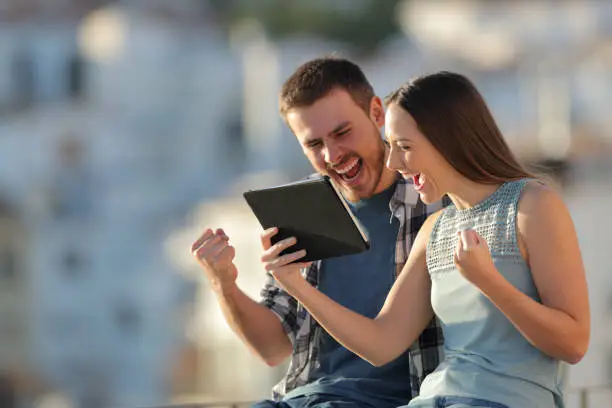 Photo of Excited couple checking tablet online content in a town